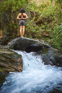 Young woman practicing yoga in a river.