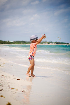 Little boy with curly hair throwing sand at a beach in the Caribbean