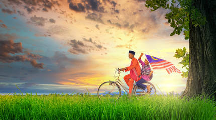 Two happy young local boy riding old bicycle at paddy field holding a Malaysian flag with beautiful sunset moments. Independence Day concept