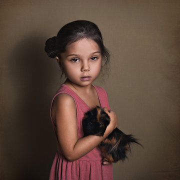 beautiful baby girl holding a fluffy Guinea pig on a paper background