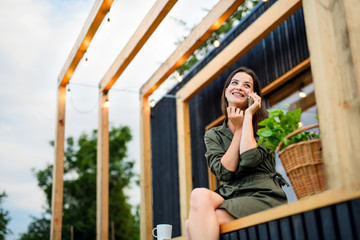 Young woman with smartphone outdoors, weekend away in container house in countryside.