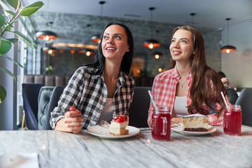 Happy smiling mother and joyful teenage daughter eating cakes and have good time together in a cafe
