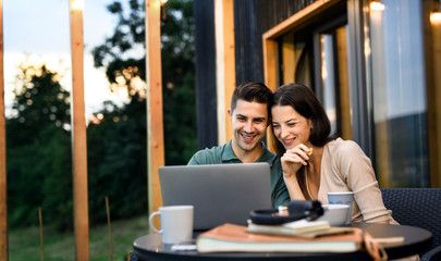 Young couple with laptop outdoors, weekend away in container house in countryside.