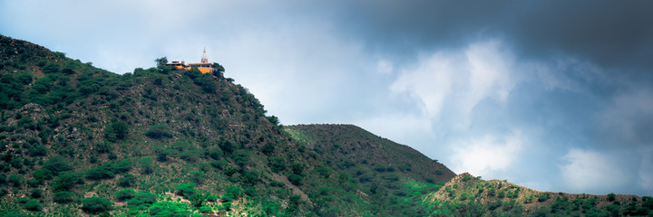 Fototapeta na wymiar hindu temple on a hill covered in vegetation with the tower and spire clearly visible in the distance with a background of dark monsoon clouds shot in Rajasthan India