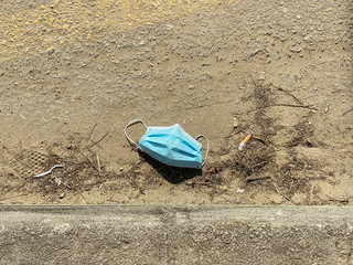 Blue medical coronavirus mask over sandy floor on the street and brush. Contamination concept