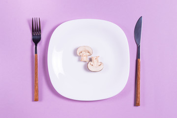 Sliced champignons on a white plate with cutlery on a purple background