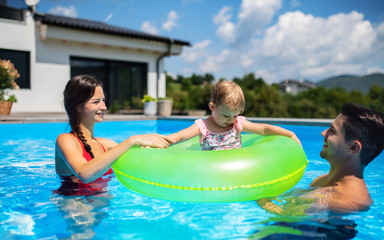 Young family with small daughter in swimming pool outdoors in backyard garden.