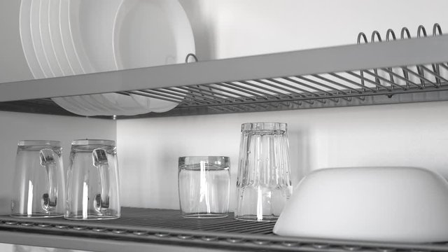 Open kitchenware drying rack with plates and cups in kitchen cabinet