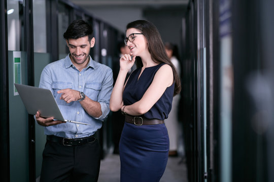 Two office employees are discussing about work outside of a meeting room and looking happily with their results.