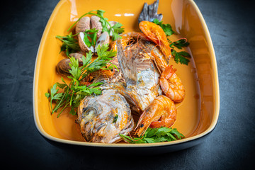Sea bream cooked with prawns and parsley in an orange baking dish.