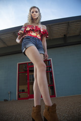 Low angle shot of a beautiful blonde female wearing an off shoulder blouse, shorts and boots