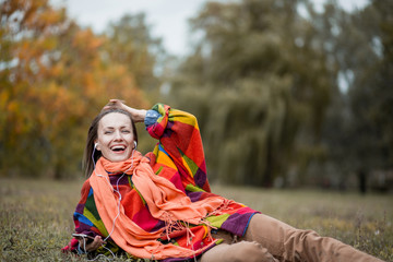 young woman in autumn park listening to music enjoying good weather wearing warm woolen clothes
