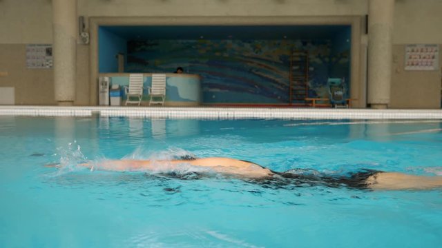 Woman in black swimsuit swims crawl in the pool.