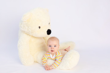 smiling baby girl 6 months old lies on a white isolated background with a large soft Teddy bear, space for text