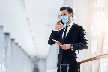 Man in suit holding passport with tickets, talking on phone