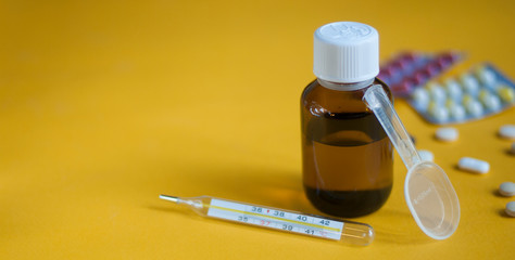 Cough syrup. Cold medicine. Pills and medicine on a yellow background. Pharmaceutical preparations...