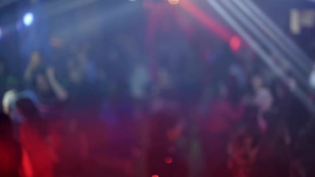 crowd of people dancing on the dance floor of a night club under the light of colored spotlights and lasers