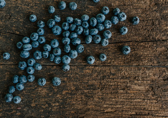Blue fresh blueberries are scattered on an old brown wooden cracked table.