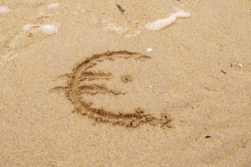 Hand written Euro sign on a yellow sand.