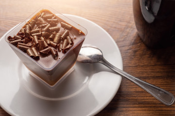 Chocolate dessert with chunks of chocolate on a white plate with tea spoon and black cup with tea on a wooden table surface. Concept desert, tea time.