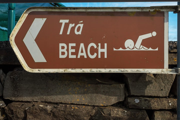 Brown sign beach in English and Irish language and pointing arrow.