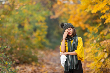 girl sneezes into a headscarf in autumn in the park. allergy or viral infection concept