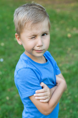 A little boy in the Park stands in a clearing and clasps his hands and winks