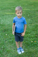 A small boy stands in a clearing, holding a large notebook. School time. Preschooler.