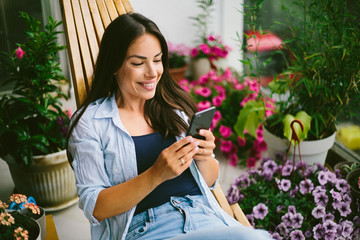 Young beautiful woman using mobile phone and relax at balcony.