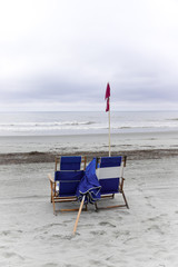 Two blue chairs on the beach beside a double red flag. Double red flags signify no one is allowed in the water due to rough water or storms in the area.