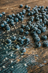 Blue fresh blueberries are scattered on an old brown wooden cracked table. Sesame seeds were poured between the fruits. Wet drops of milk on the table. basil leaves, green fresh seasoning.