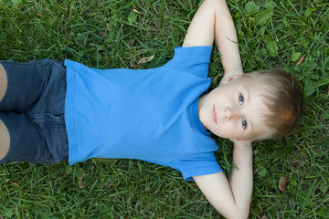 Pre-teen boy lying on back in grass, hands behind head, elevated view.