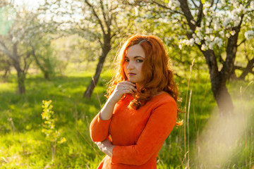 Portrait of a red-haired girl walking in an apple orchard in an orange dress