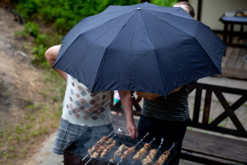 Men barbecue in the rain under an umbrella