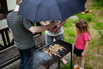 People barbecue in the rain under an umbrella