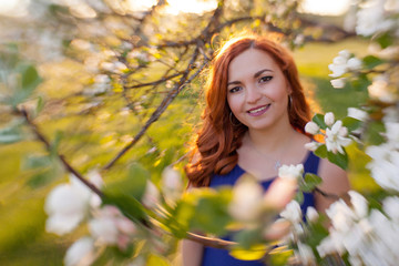 Tiltshift Portrait of a red-haired girl walking in an apple orchard in an blue dress
