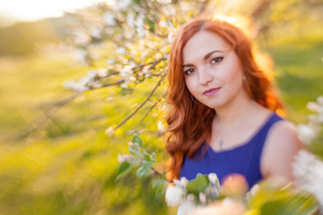 Tiltshift Portrait of a red-haired girl walking in an apple orchard in an blue dress