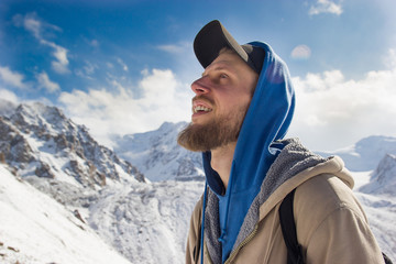 Fototapeta na wymiar A bearded guy among snow mountains rejoices in life.