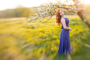 Fototapeta na wymiar Tiltshift Portrait of a red-haired girl walking in an apple orchard in an blue dress