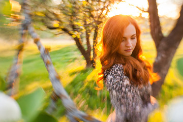 Tiltshift Portrait of a red-haired girl walking in an apple orchard in an bright dress