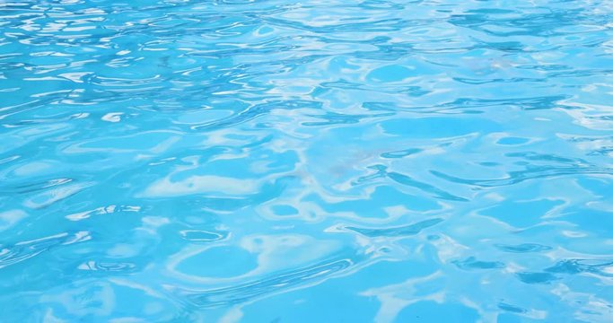 Ripples on the surface of the transparent blue water in a pool background.