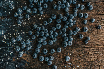 Blue fresh blueberries are scattered on an old brown wooden cracked table. Sesame seeds were poured between the fruits. Wet drops of milk on the table. basil leaves, green fresh seasoning.