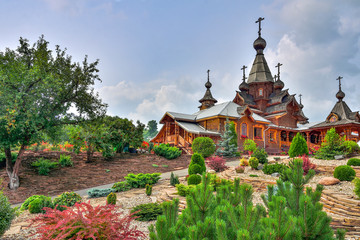 Naklejka premium Stony garden with different dwarf evergreen conifers near wooden Christian Temple