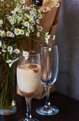Cold latte, coffee with milk and ice in beautiful glass on dark background with small flowers daisy.