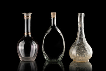 Glassware on a black isolated background. Decanters of various shapes. A group of transparent items. The reflection under the objects. Old household items. Fragile dishes. Liquid containers.