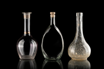 Obraz na płótnie Canvas Glassware on a black isolated background. Decanters of various shapes. A group of transparent items. The reflection under the objects. Old household items. Fragile dishes. Liquid containers.