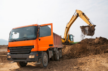 Obraz premium Loading of earth soil into the body of a cargo dump truck by an excavator bucket