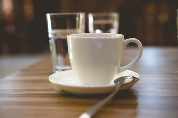 white cup of coffee on the table and two glass of water, cup of tea in a white cup with spoon at...