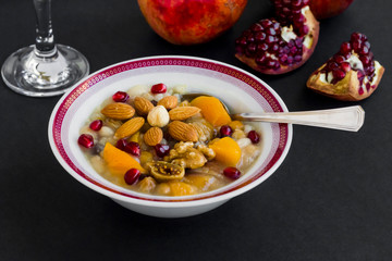 Traditional Turkish Dessert Asure or Noah's Ark Pudding designed in white bowl,on black surface with sliced pomegranate fruit