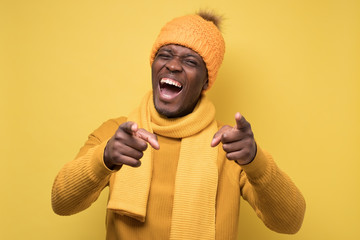 African man in yellow sweater and warm hat pointing at camera on joke